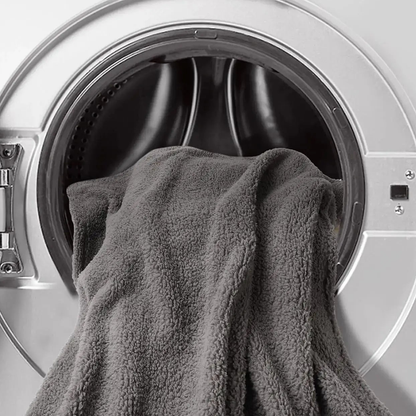 Gray sherpa blanket hanging out of the open door of a front-loading washing machine