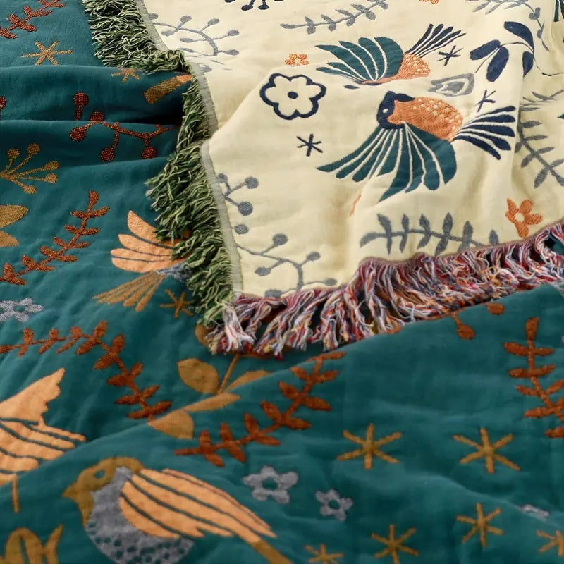 A corner of the throw with the cream side folded over the teal side, a green fringe on one edge and a pink, cream and blue fringe on the other