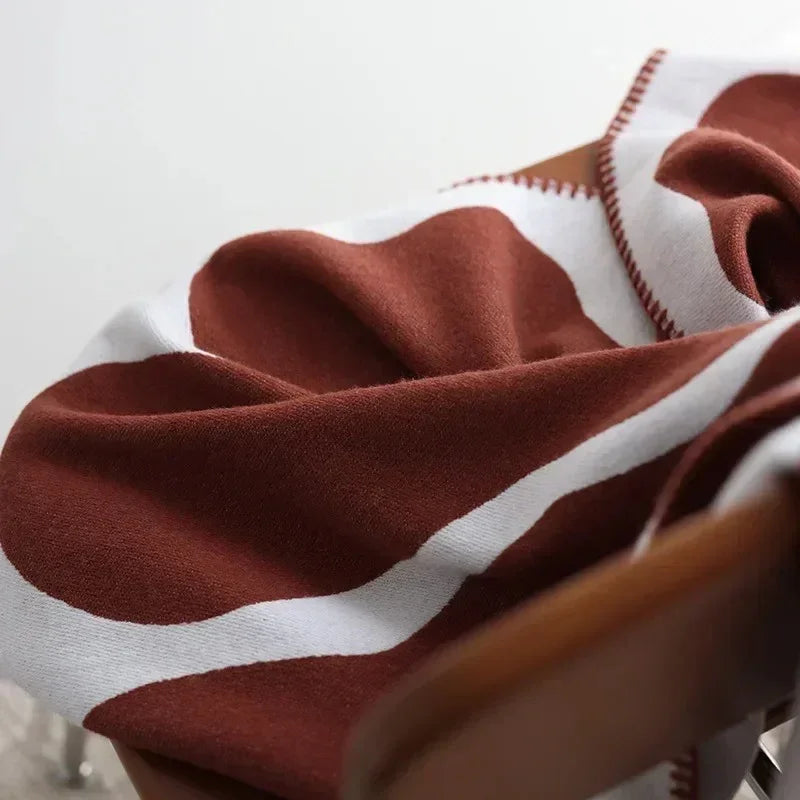 A close view of the soft knit face of a rust and off-white throw blanket draped over a wooden seat back.