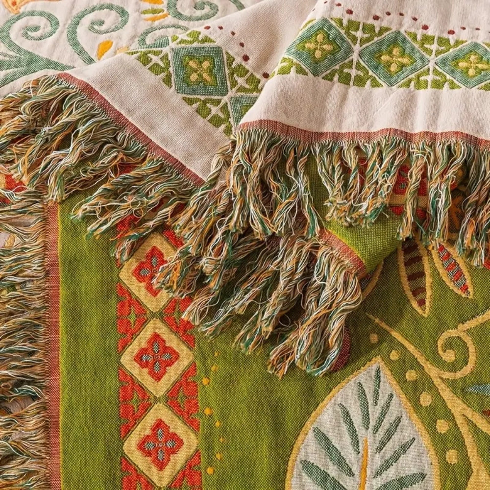 A close-up of the tasseled end of the throw, showing the diamond strip on the cream side and a large pale leaf on the olive reverse