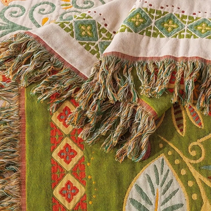 A close-up of the tasseled end of the throw, showing the diamond strip on the cream side and a large pale leaf on the olive reverse