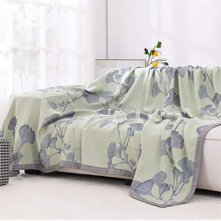 Green ginkgo leaf quilt draped over a cream sofa, with the gray border along its edge