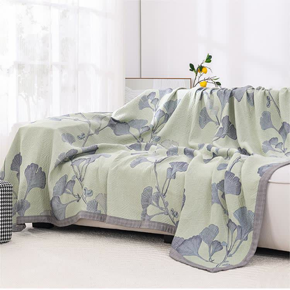 Green ginkgo leaf quilt draped over a cream sofa, with the gray border along its edge
