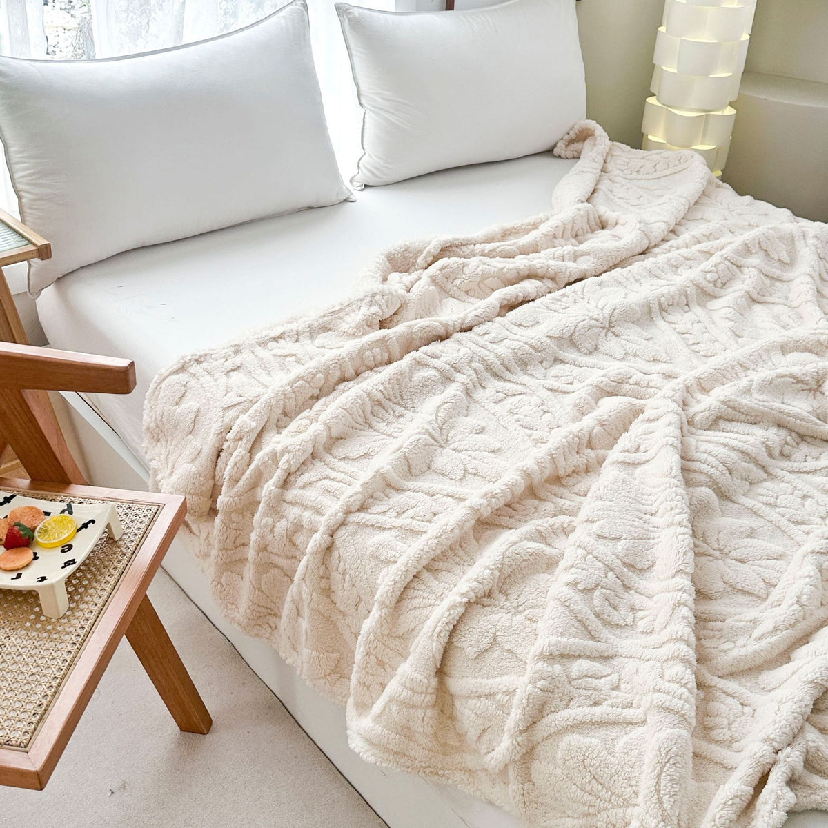 Ivory fleece blanket spread across a bed beside a low side table