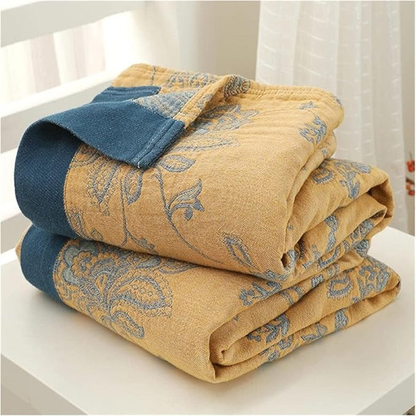 Mustard throw blanket folded in a stack, close view of the woven flowers, the stitched border and the layered cotton gauze edge