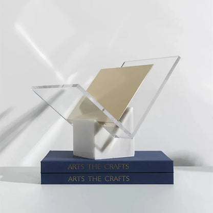 White marble magazine holder with a gold-toned divider in its clear acrylic V, on two navy books in sunlight