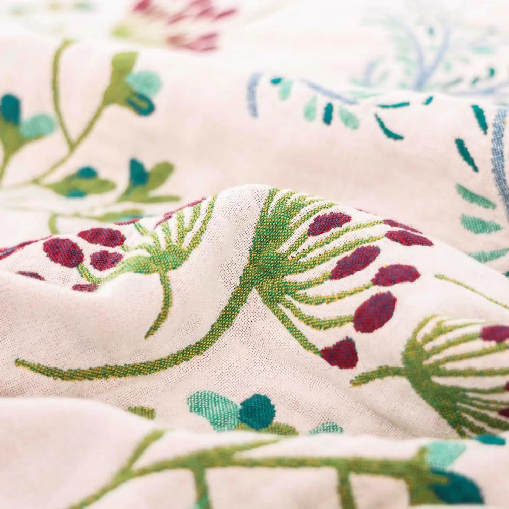 Close-up of burgundy seed heads and green stems woven into the cream cotton gauze