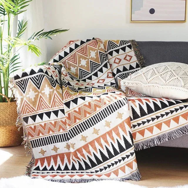 A cream and tan jacquard throw with black zigzags and triangles, draped over a gray couch
