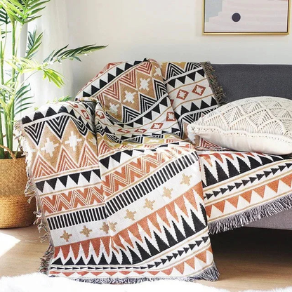 A cream and tan jacquard throw with black zigzags and triangles, draped over a gray couch