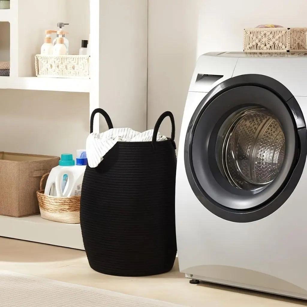 A black rope laundry hamper full of laundry next to a front-loading washer.