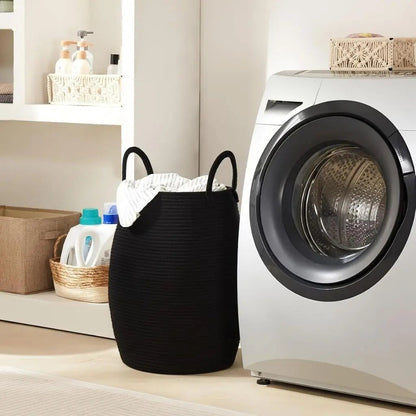 A black rope laundry hamper full of laundry next to a front-loading washer.