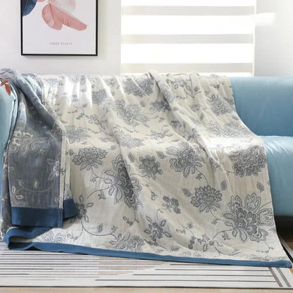 Blue floral jacquard throw blanket over a sofa, gray-blue flowers on a cream face with a blue border