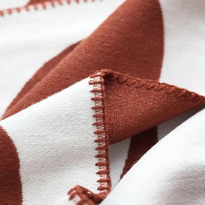 A close view of a folded corner of a rust and off-white knit throw blanket and its looped stitched edge.
