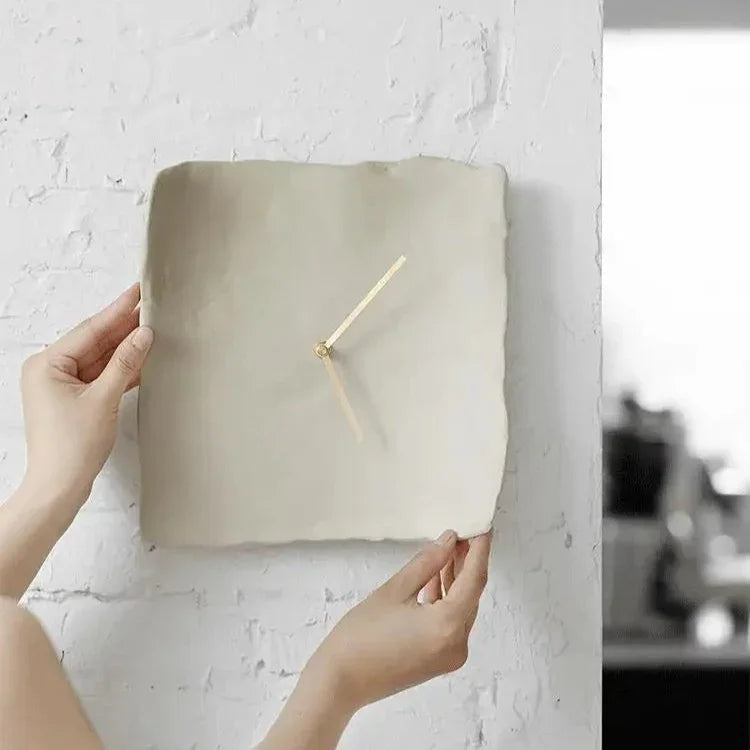 Two hands holding the white crumpled resin wall clock flat against a whitewashed brick wall