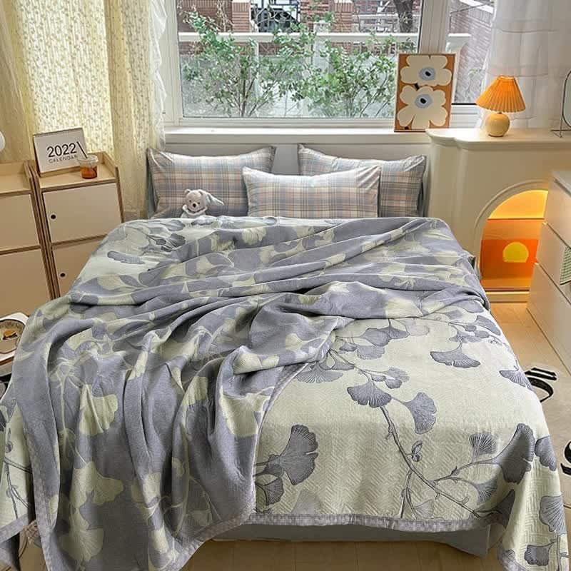 Green ginkgo leaf quilt rumpled over a bed, half turned over to show the slate gray reverse with pale leaves