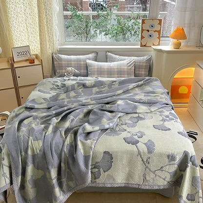 Green ginkgo leaf quilt rumpled over a bed, half turned over to show the slate gray reverse with pale leaves
