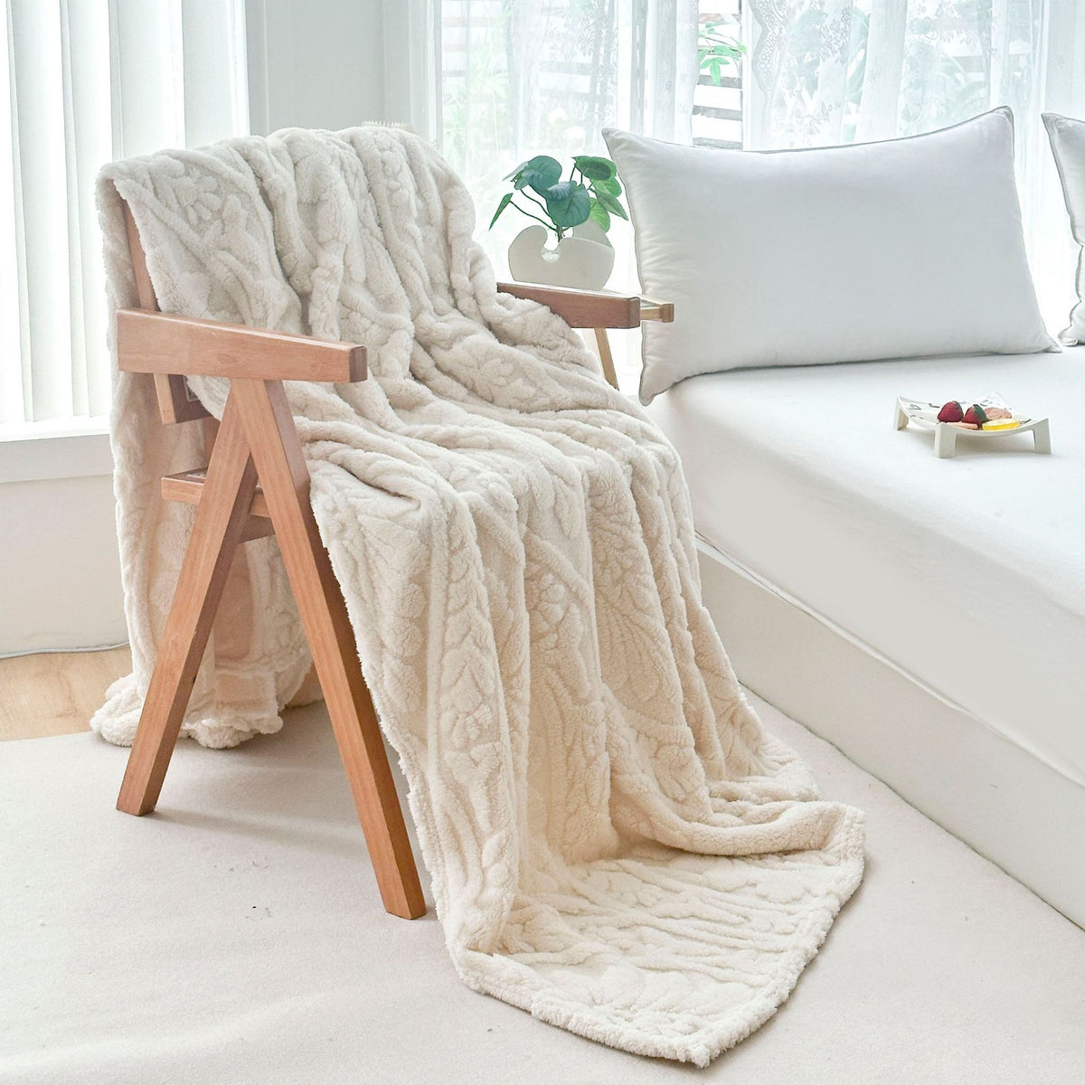 Ivory fleece blanket draped over a wooden armchair by the bed