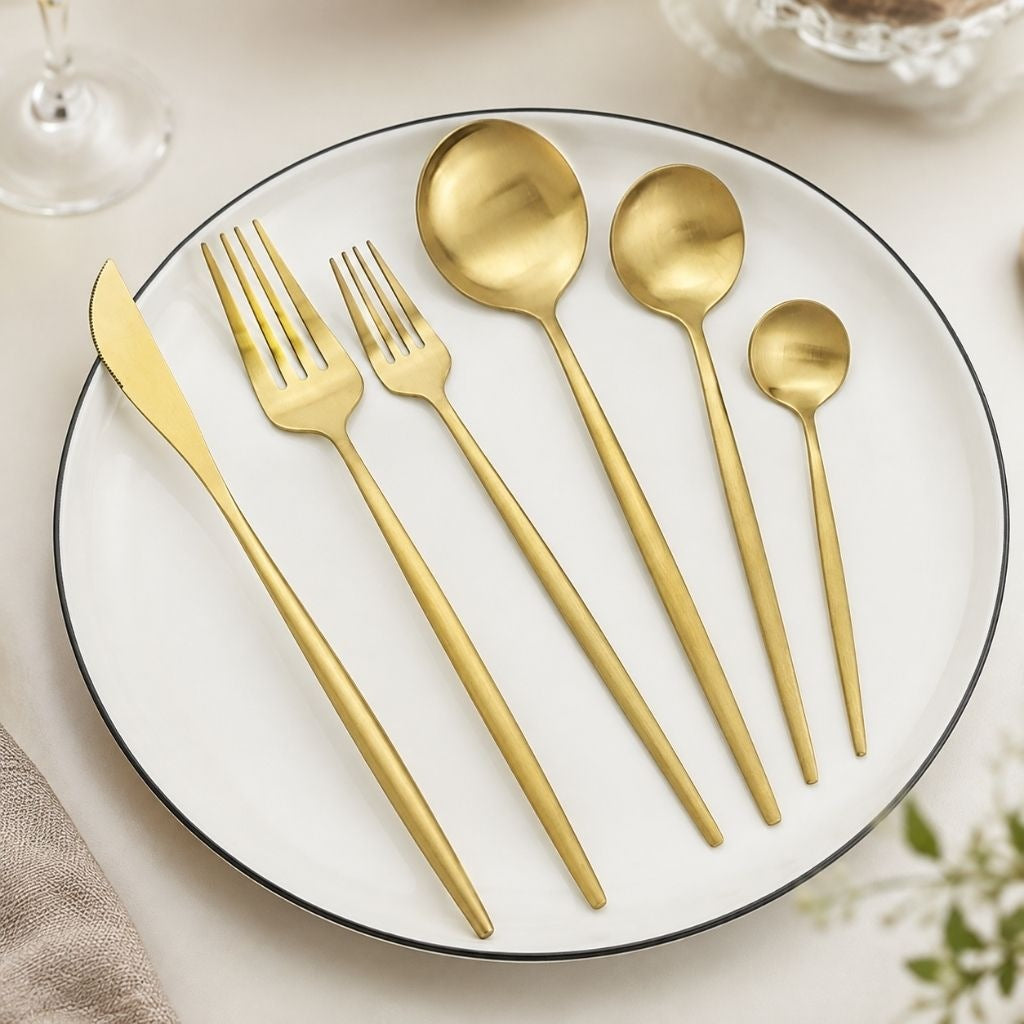 Matte gold cutlery place setting on a white plate: six pieces from dinner knife to teaspoon