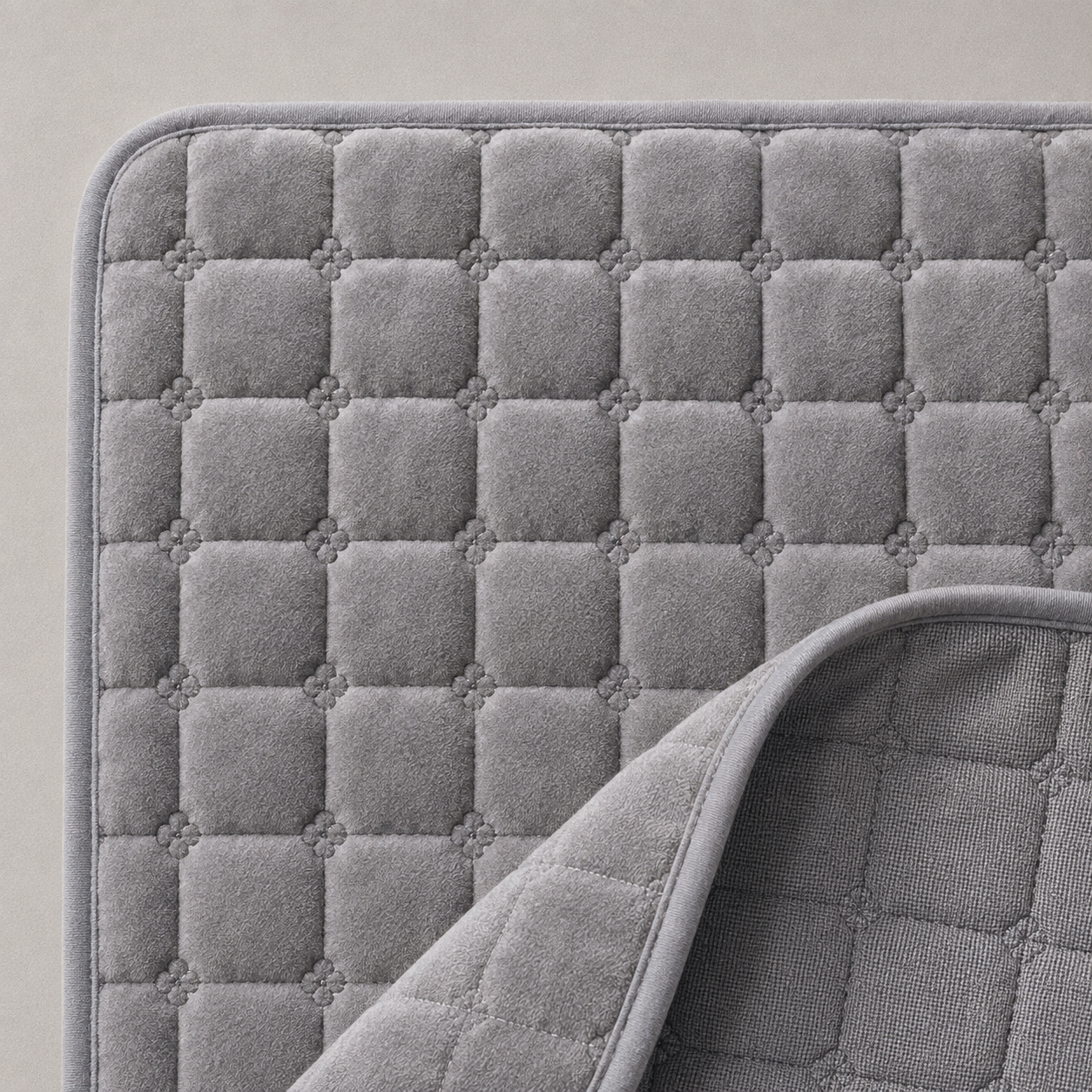 Close up of the gray quilted fabric showing the square quilt grid with a four lobed stitch knot at each intersection, the bound edge, and one corner turned back to show the reverse