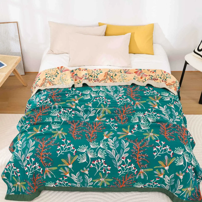 Teal wildflower gauze blanket spread over a bed, with the apricot floral reverse showing at the pillows and a dark green band along the foot