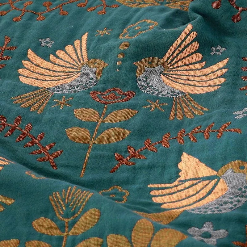 A close-up of the teal side, showing pairs of golden birds with gray speckled bodies, a flower on a stem and rust red sprigs woven into the cotton