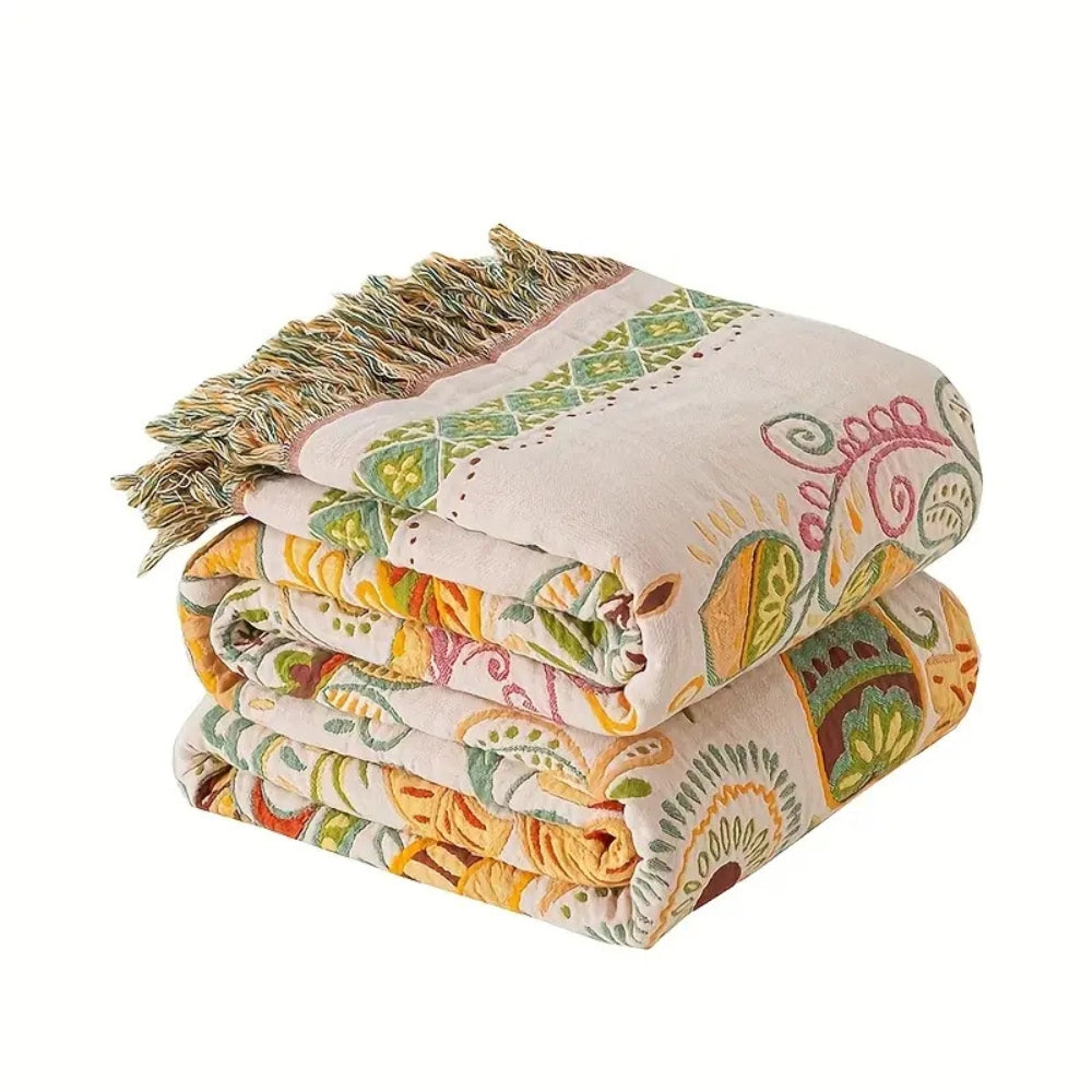 The leaf and paisley throw blanket folded into a stack, showing its cream face, a strip of small diamonds and the tassel fringe
