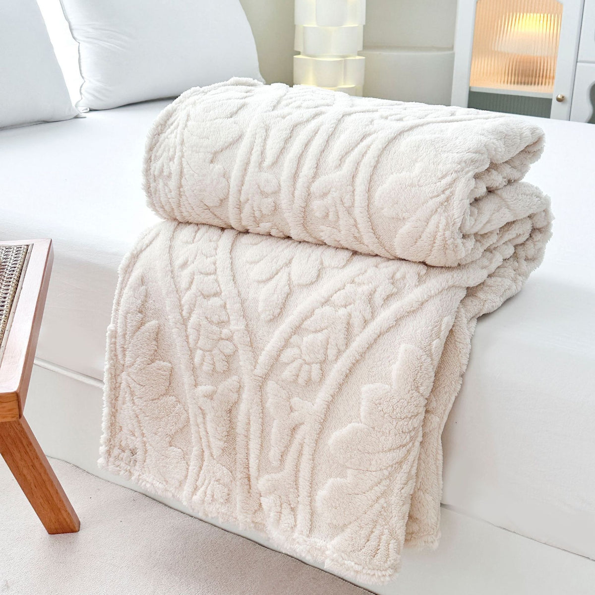Ivory embossed fleece blanket folded and rolled on a bed