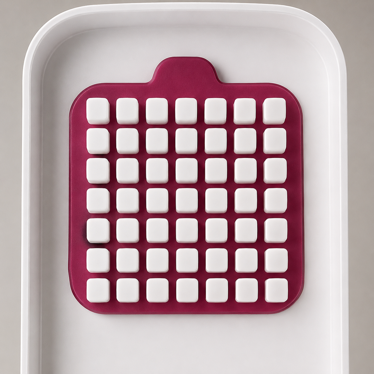 Close-up of the deep pink pad inside the lid, carrying seven rows of seven flat-topped white pegs that line up with the blade grid.