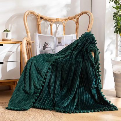 A teal flannel throw with raised stripes and teal pom-poms over a rattan armchair