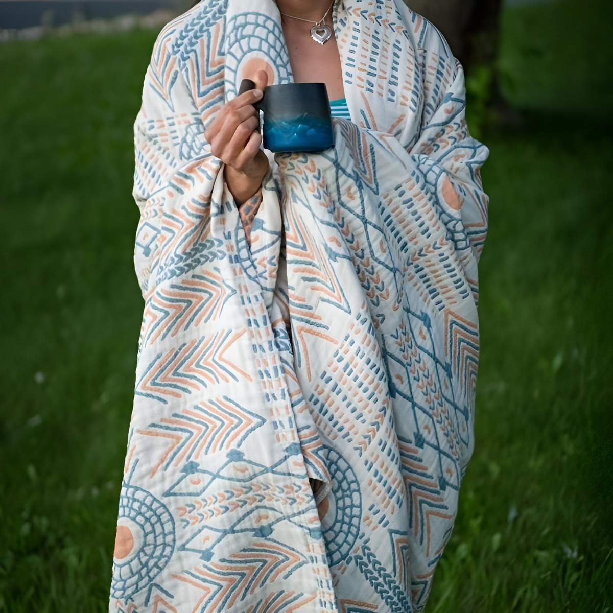 Person wrapped in the reversible boho blanket outdoors, holding a mug