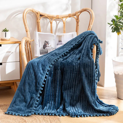 A blue flannel throw with raised stripes and blue pom-poms along the edge, over a rattan armchair