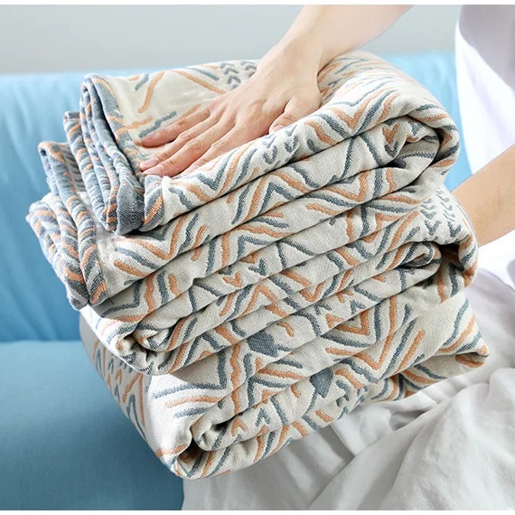 Cotton muslin blanket folded into a stack, chevron pattern in orange and blue-gray on cream