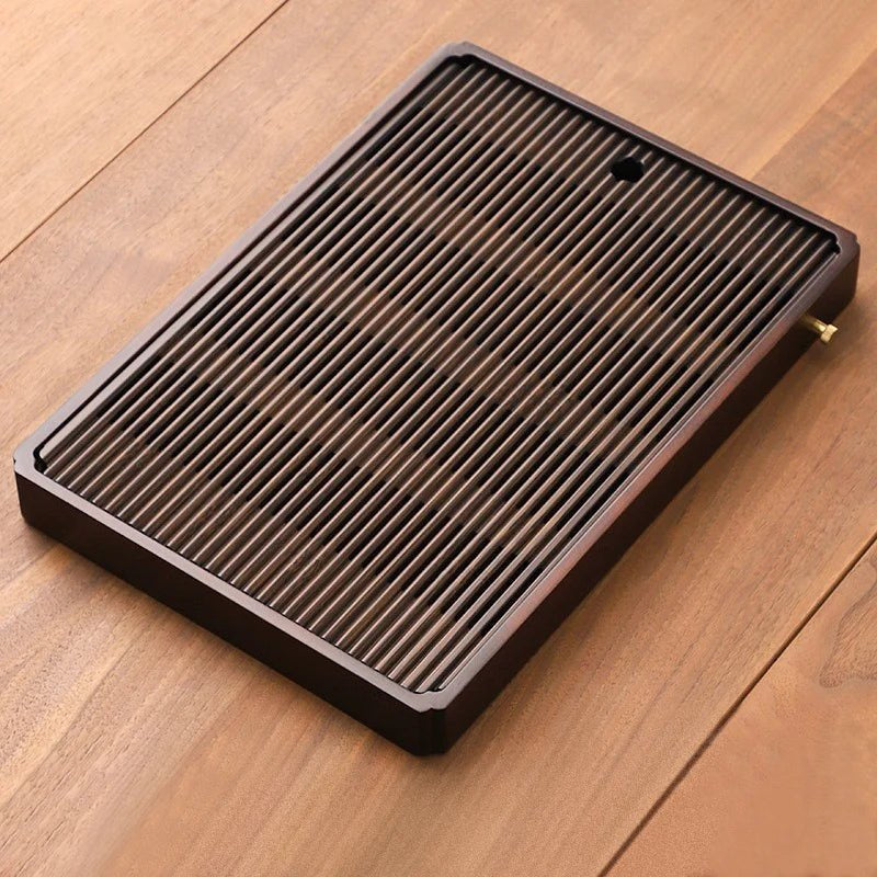 Large slatted bamboo tea tray in a dark brown finish on a wooden table, the drain cap on its long side.