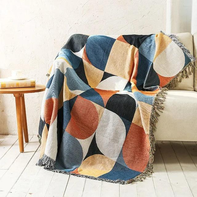 A jacquard throw of large half and quarter circles in navy, rust, cream and mustard, over a cream couch