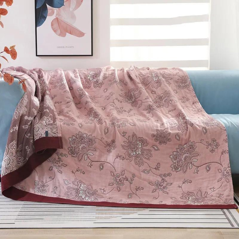 Pink floral jacquard throw blanket over a sofa, deeper rose flowers on a dusty pink face with a burgundy edge