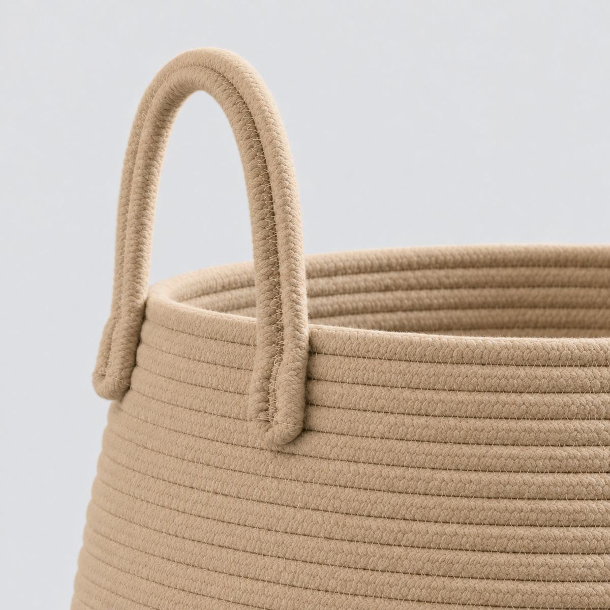 A close view of a tan rope handle stitched to the outside of the hamper below the rim, above rows of rope.