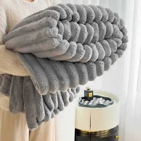 Gray faux rabbit fur throw rolled up in someone's arms, its pleats forming plump round rolls
