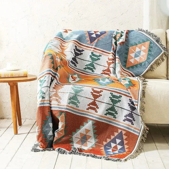 An orange and cream banded jacquard throw with teal and green hourglass shapes and diamonds, over a cream couch