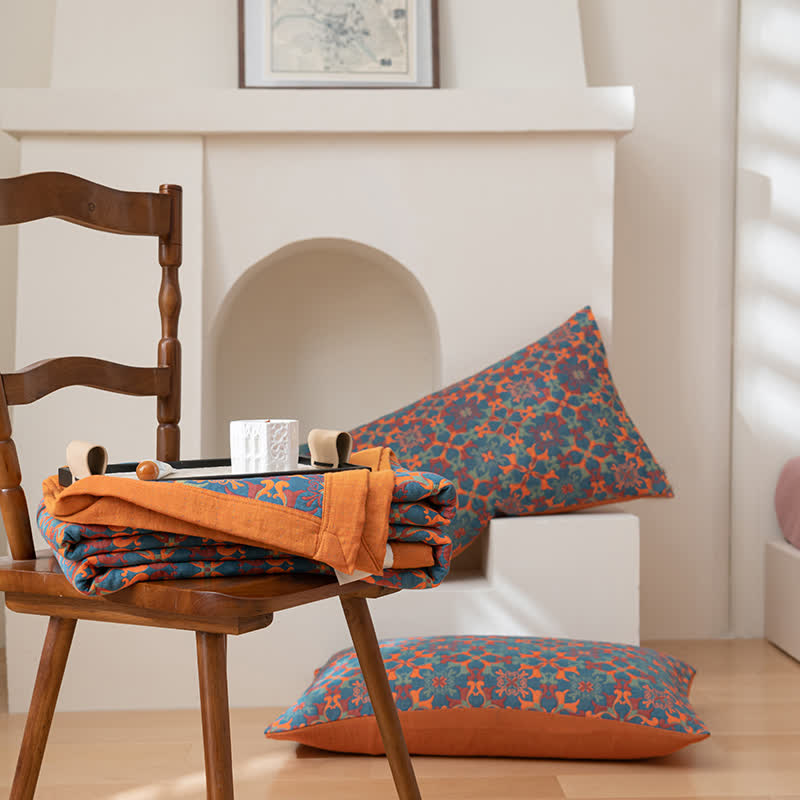 Two pillowcases in the orange and blue pattern, one on a wooden chair beside the folded quilt and one on the floor