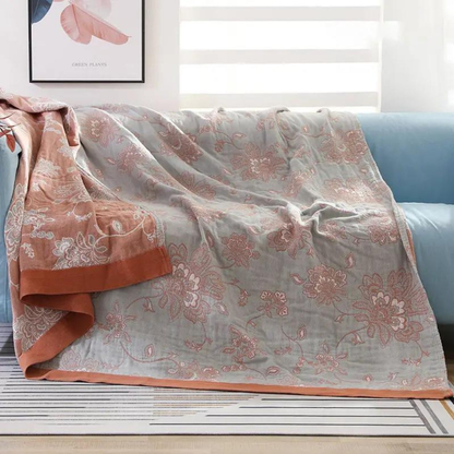 Rust floral jacquard throw blanket over a sofa, coral flowers on a light gray face with a rust border