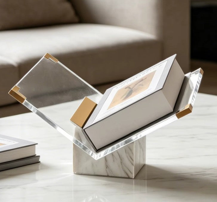 White and gold marble book stand with gold-toned corner caps holding a boxed book on a marble coffee table