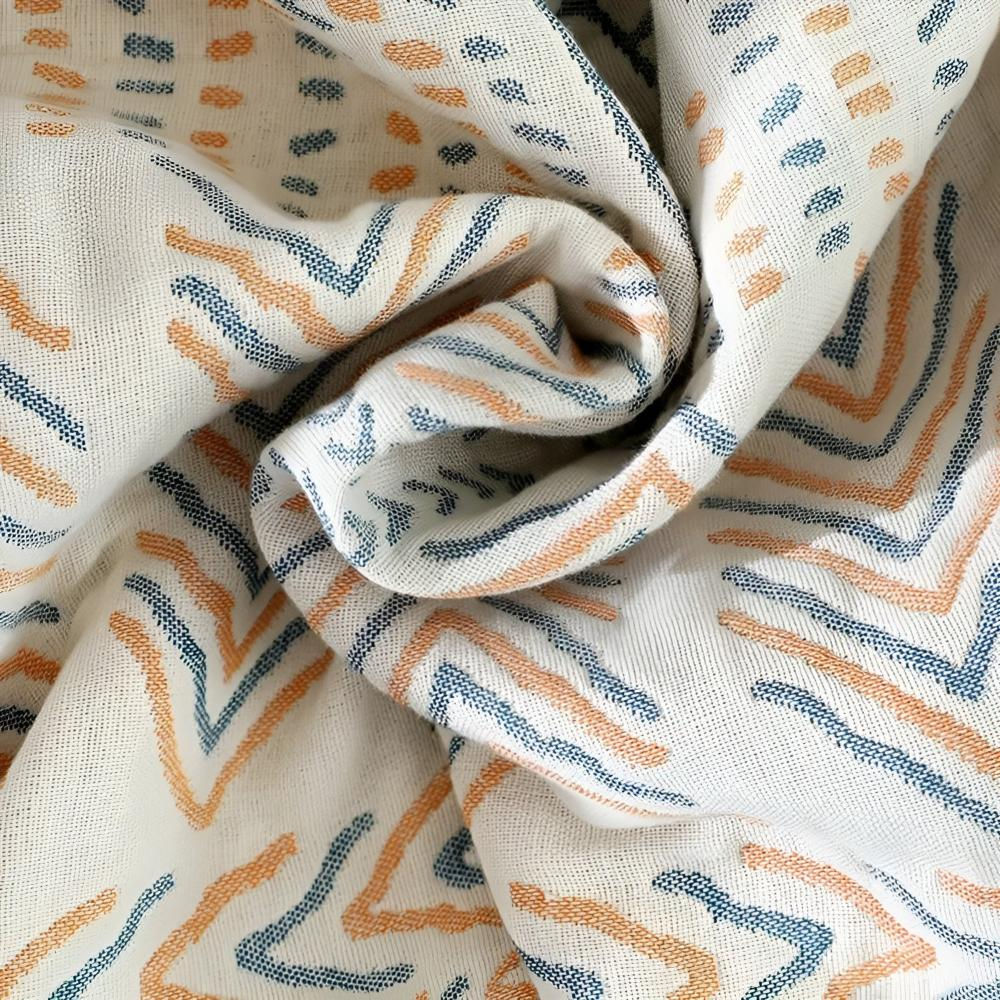 Close-up of the cream face swirled into folds, woven orange and blue chevrons and dashes in cotton muslin