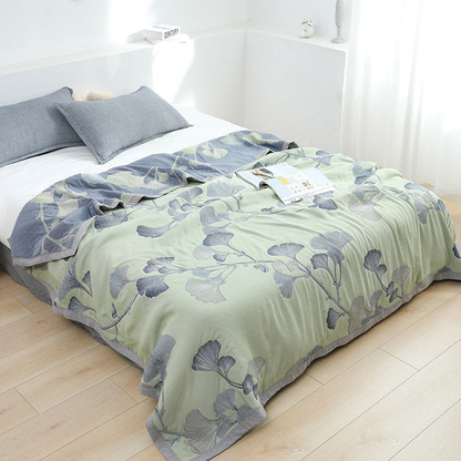 Green ginkgo leaf gauze quilt spread over a bed, with its slate gray reverse folded back at the pillows