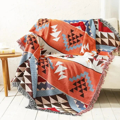 An orange jacquard throw with white and black triangles and blue stepped diamonds, draped over a white couch