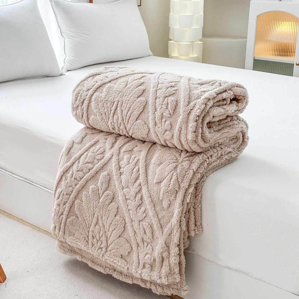 Beige embossed fleece blanket folded and rolled on a bed