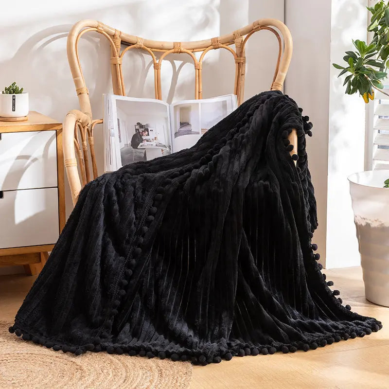 A black flannel throw with raised stripes and a black pom-pom edge over a rattan armchair