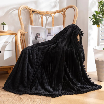 A black flannel throw with raised stripes and a black pom-pom edge over a rattan armchair