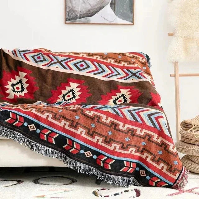 A red and brown jacquard throw with red medallions and a band of arrows, spread over a cream couch