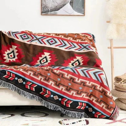 A red and brown jacquard throw with red medallions and a band of arrows, spread over a cream couch
