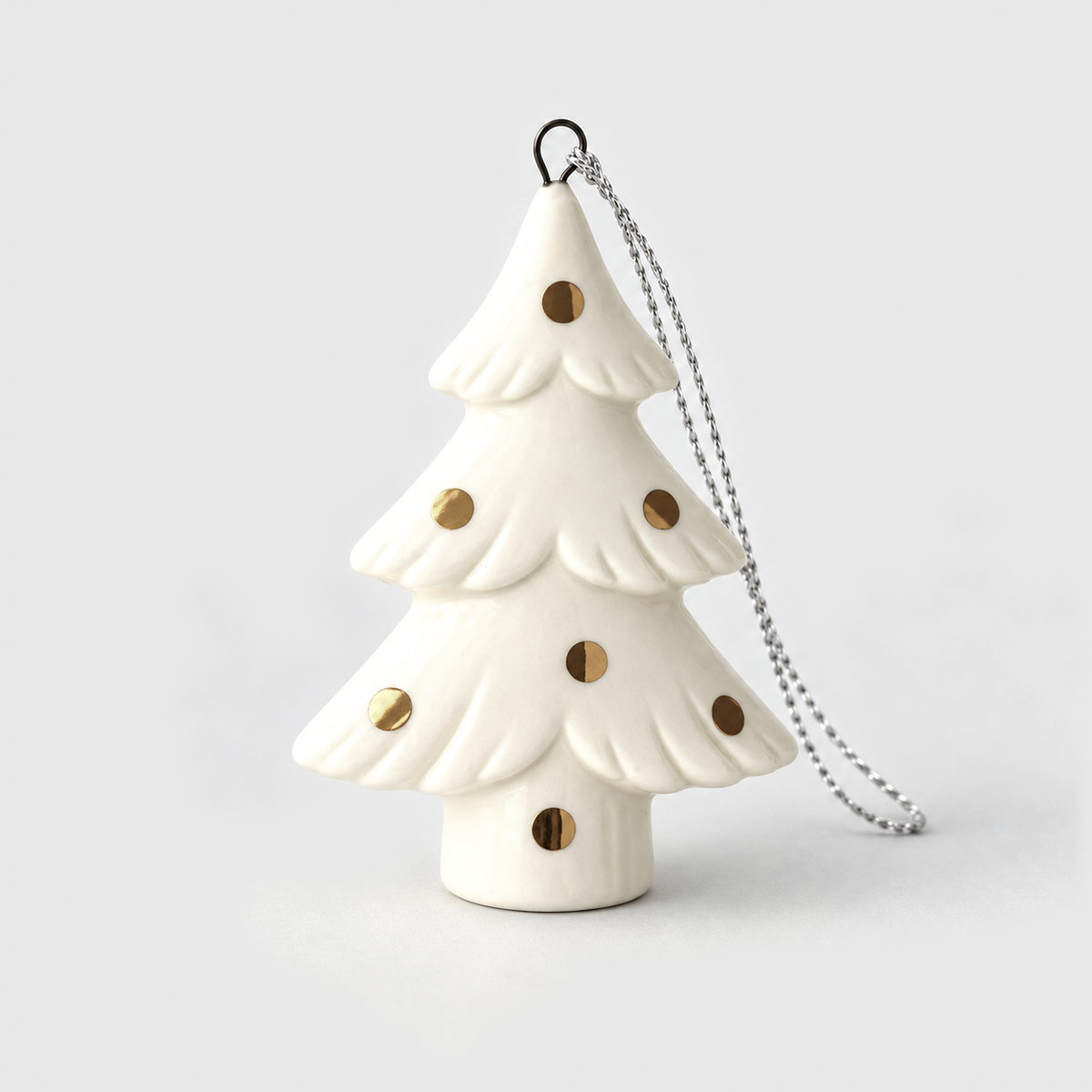 White ceramic Christmas tree ornament in the Polka Dot style, three scalloped tiers with round gold dots on a short trunk, on a light gray background